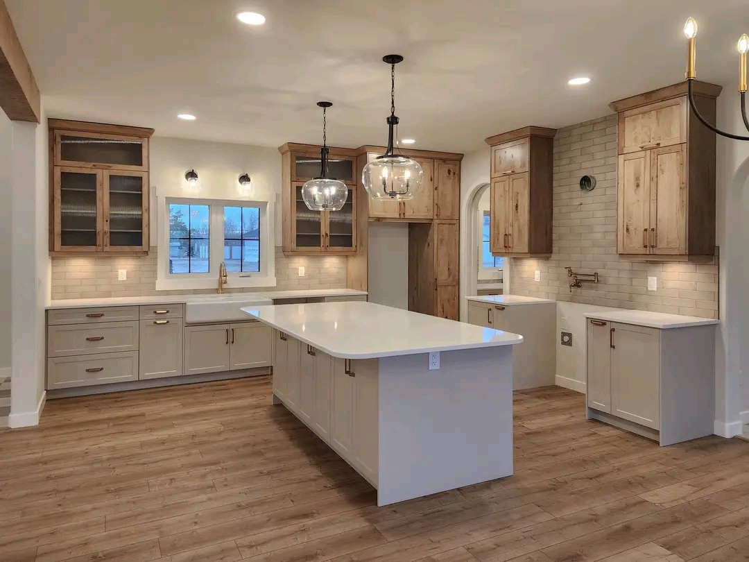 Spacious kitchen with light wood floors, two pendant lights over a large island, cream cabinets, wood accents, and warm under-cabinet lighting.