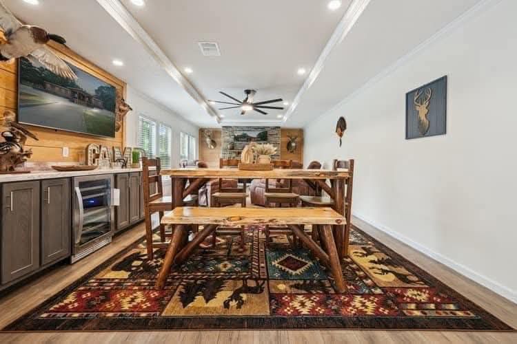 A cozy dining room featuring a rustic wooden table with benches, colorful patterned rug, animal decor, modern ceiling fan, and side cabinets with a TV.