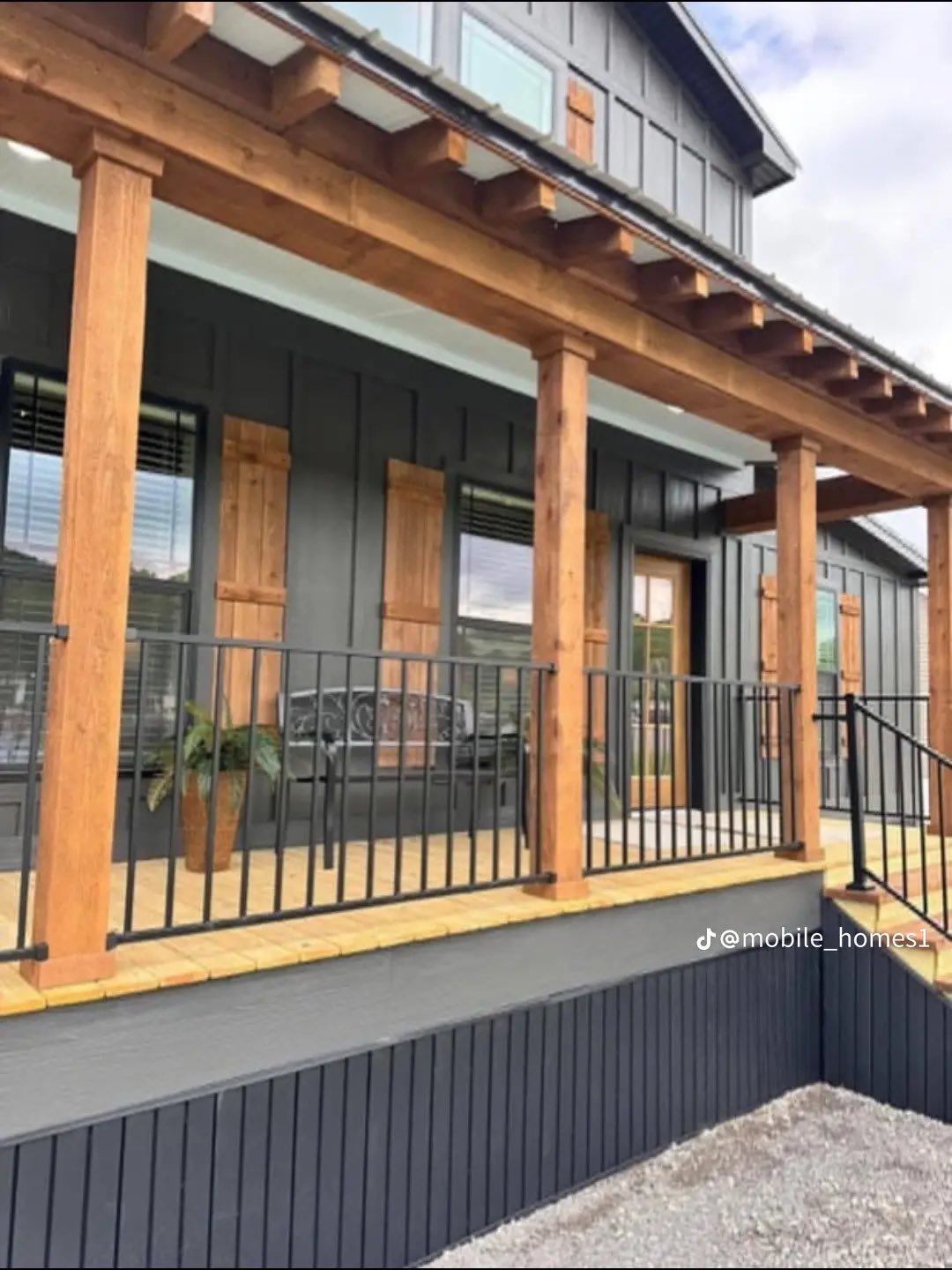 Front view of a modern house with dark gray siding, wooden shutters, and a welcoming porch with wooden columns and black railings, conveying a cozy atmosphere.