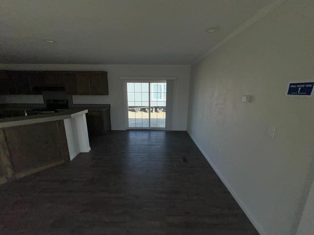 A small, empty room with dark hardwood floors, white walls, and a sliding glass door leading outside. A kitchen with wooden cabinets is in the corner.