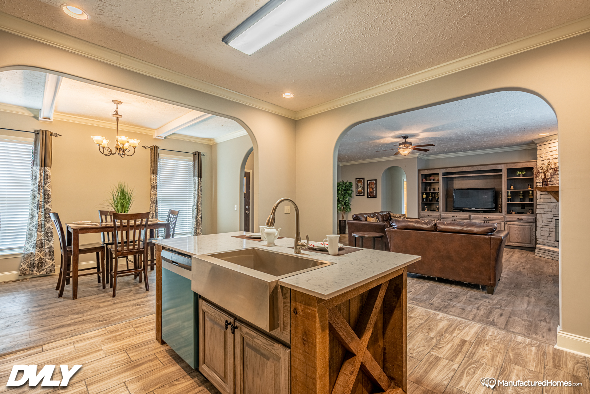 Spacious open-plan kitchen and living area with wood floors. Features a central island, farmhouse sink, and cozy living room with a large TV unit.