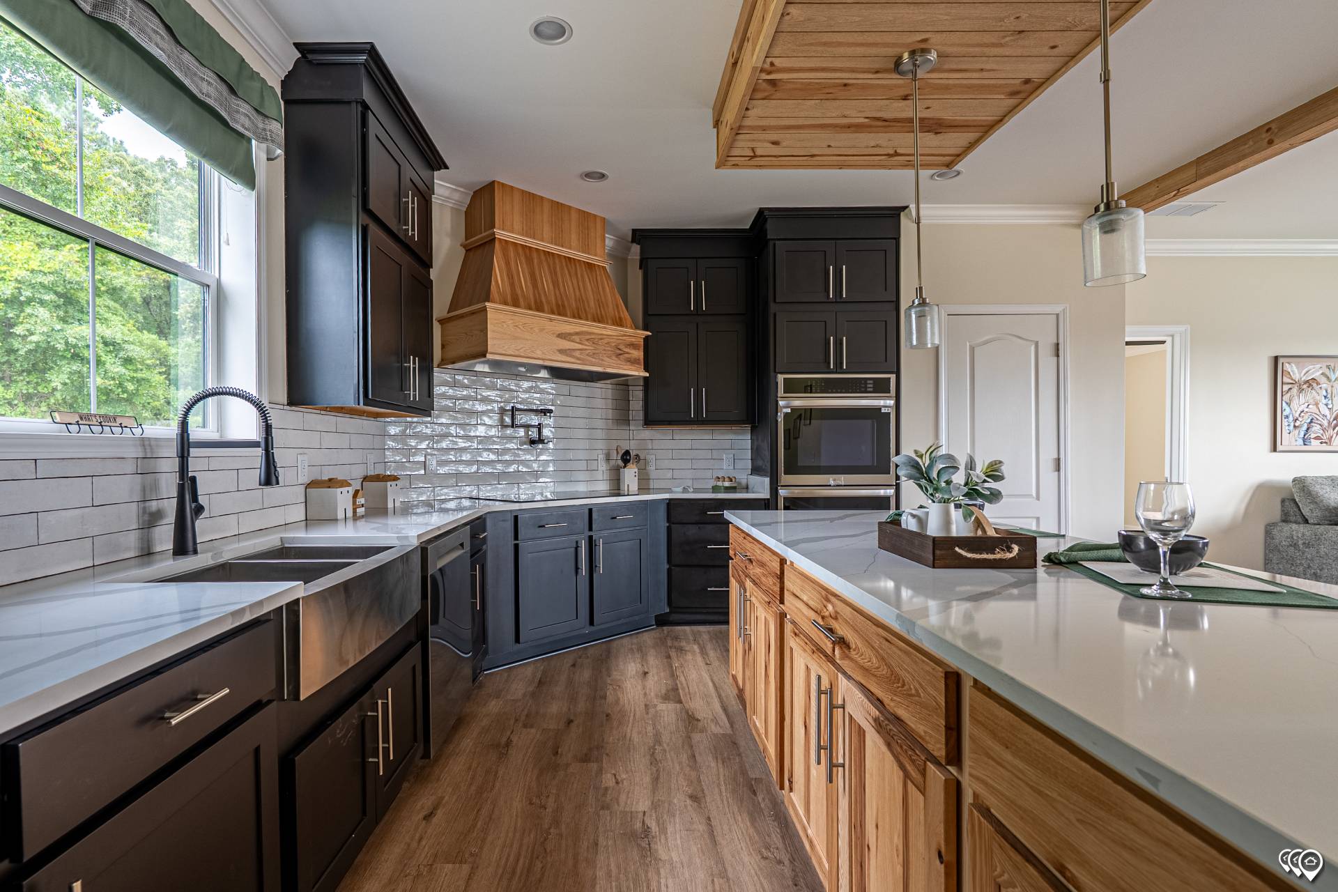 Modern kitchen with black and wood cabinetry, white countertops, and stainless steel sink. A tray with wine glasses sits on the island, evoking a cozy and inviting atmosphere.