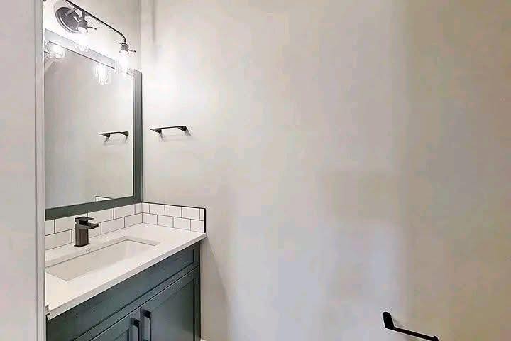 Small, minimalist bathroom with a dark vanity, white countertop, and subway-tiled backsplash. Silver faucet, wall-mounted light, and towel holder add sleekness.
