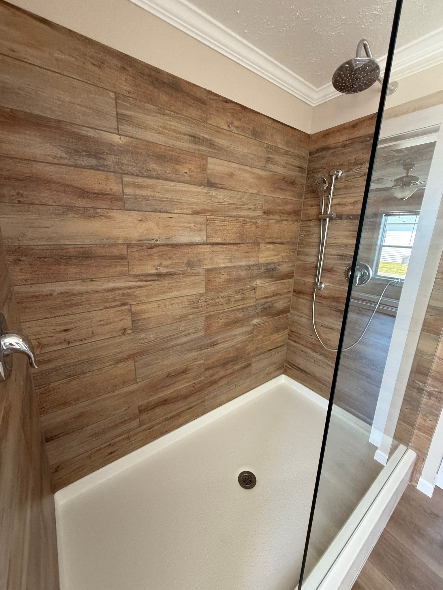 Modern shower with wood-patterned tiles, glass door, and silver fixtures. The bright space conveys a clean, rustic, and inviting atmosphere.