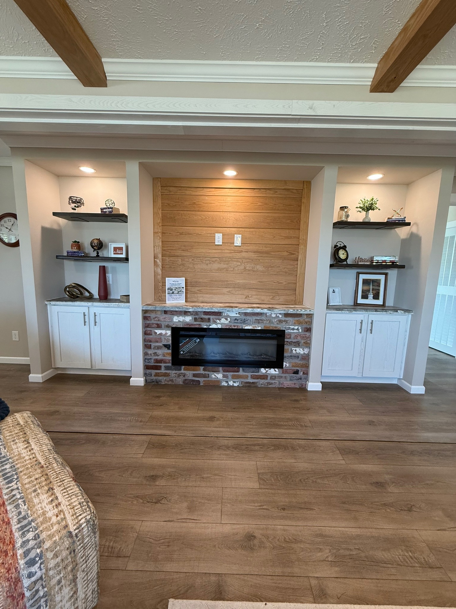 Stylish living room with a brick and wood fireplace, flanked by white shelves and cabinets. Warm lighting creates a cozy atmosphere.