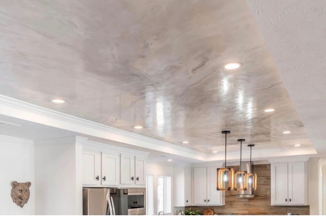 Modern kitchen with glossy marble ceiling reflecting warm light. Elegant pendant lights hang above white cabinets and stainless steel appliances, creating a sleek, inviting ambiance.