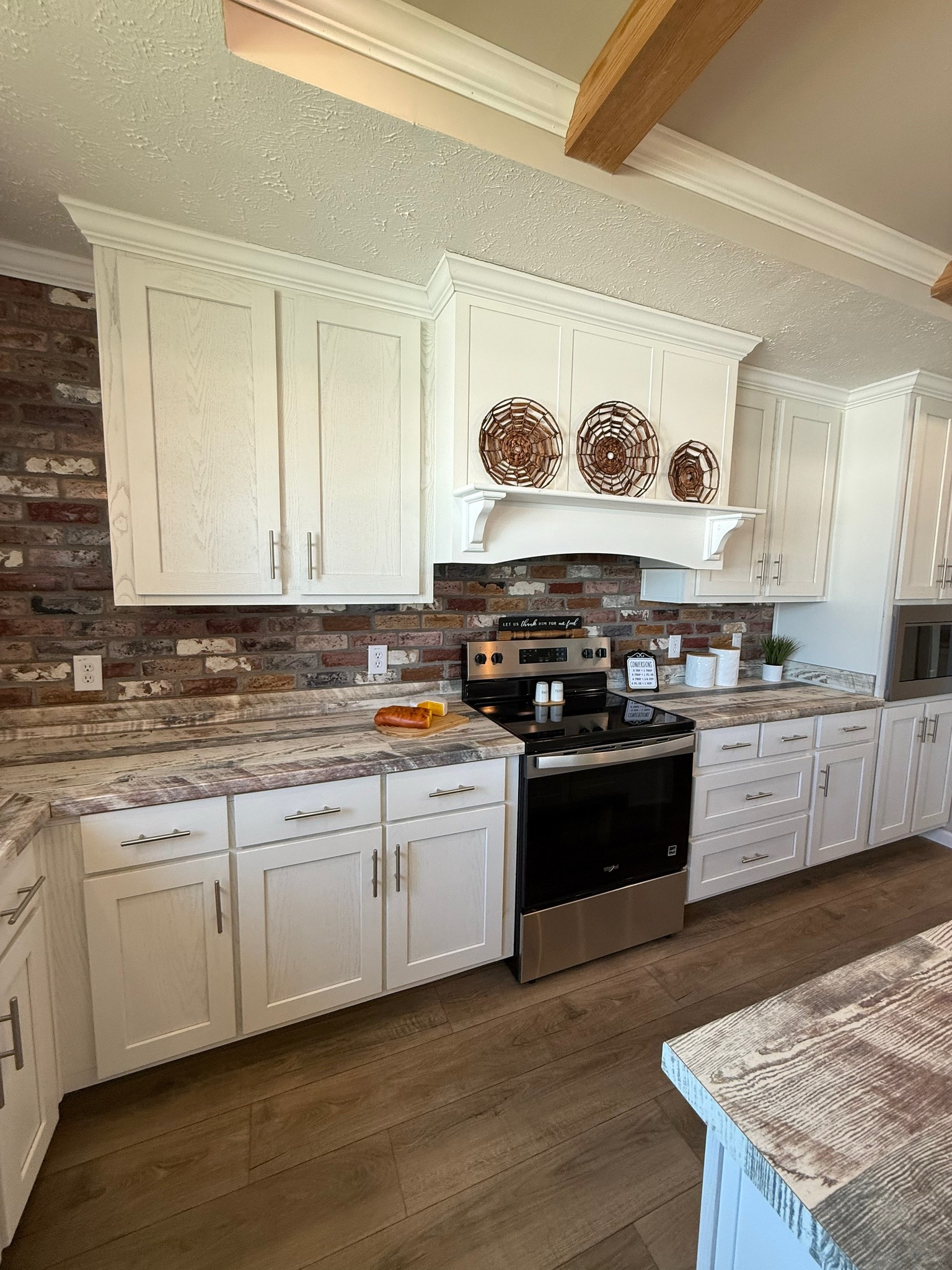 Modern kitchen with white cabinets, stainless steel stove, and brick backsplash. Decor includes woven baskets and small plants, creating a cozy vibe.