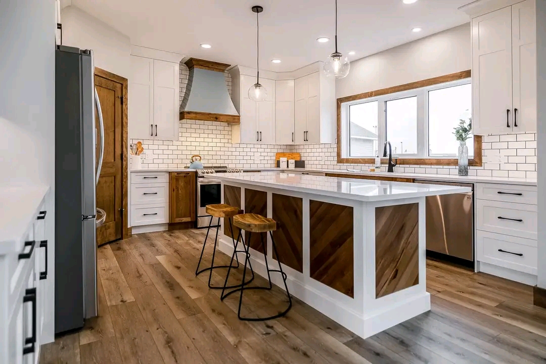 Sleek kitchen with white cabinets, brick backsplash, and wooden accents. A large island with stools, pendant lights above, and hardwood floors.