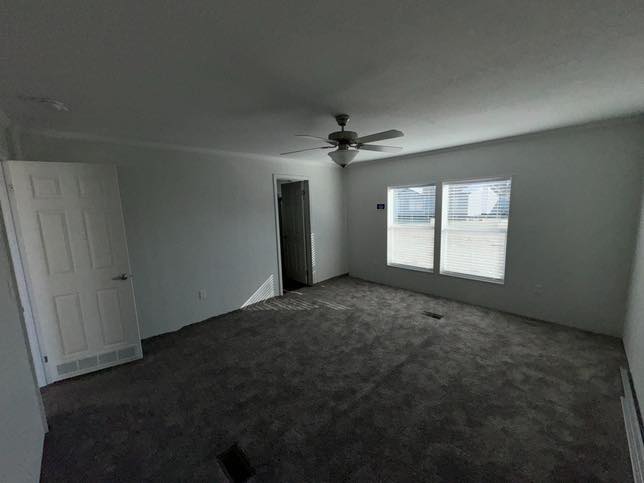 Empty room with gray carpet and white walls, featuring a ceiling fan, two windows with blinds on the right, and an open door on the left.