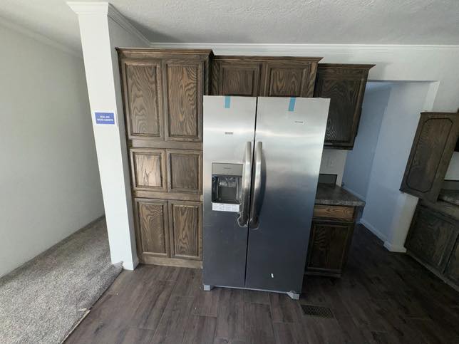 The image shows a modern stainless steel refrigerator with a water dispenser, surrounded by dark wood cabinets in a kitchen with dark wood flooring.