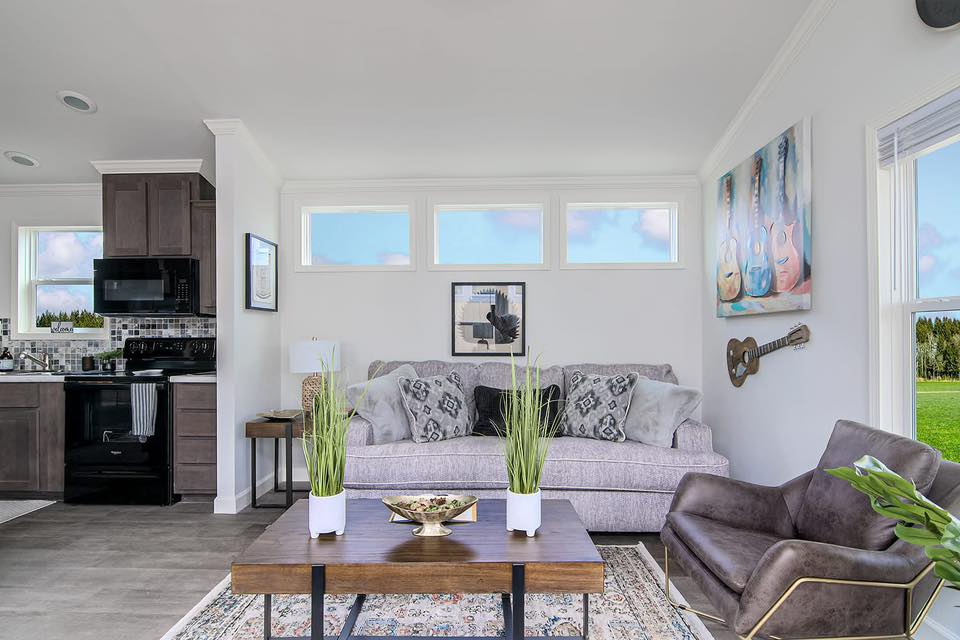 A cozy living room with a light gray sofa adorned with patterned cushions, a wooden coffee table with plants, guitar artwork, and a wall-mounted guitar. Bright and inviting.