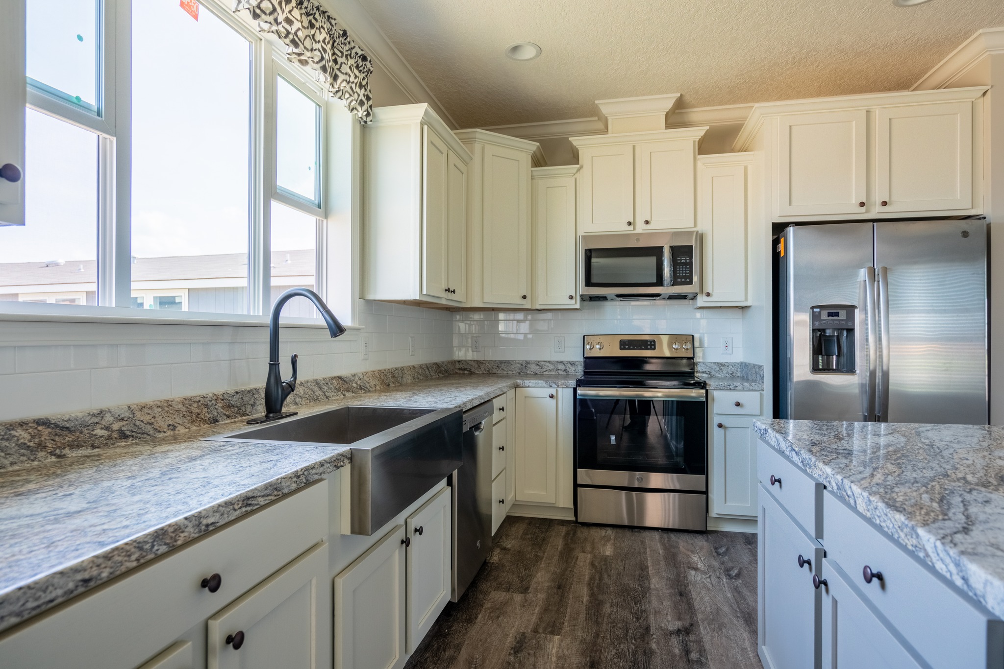 Bright kitchen with white cabinets, stainless steel appliances, and granite countertops. Large windows and a farmhouse sink enhance its modern charm.