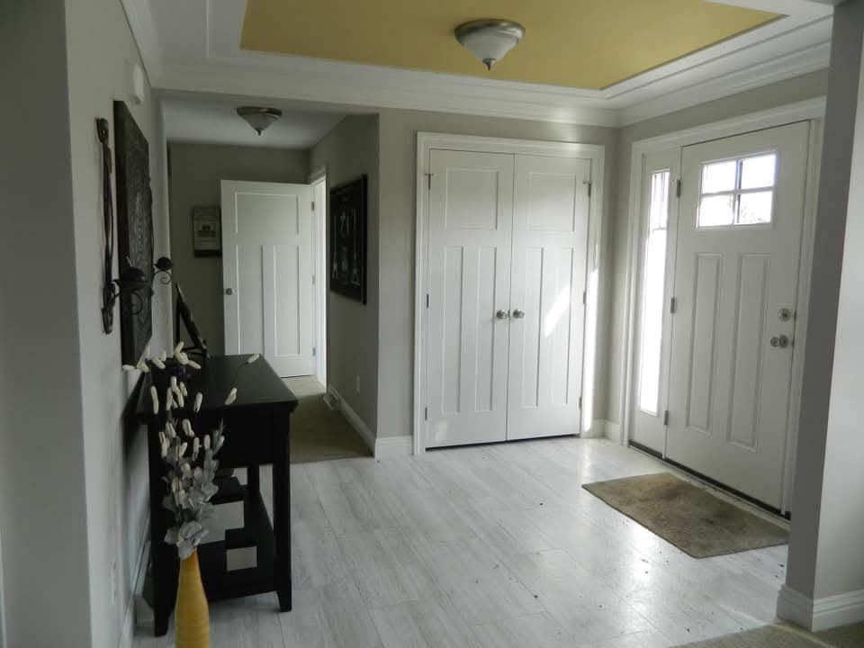 Bright hallway with light gray walls and white wooden doors. Sunlight streams through a window, illuminating a console table with decorative items. Cozy and inviting.