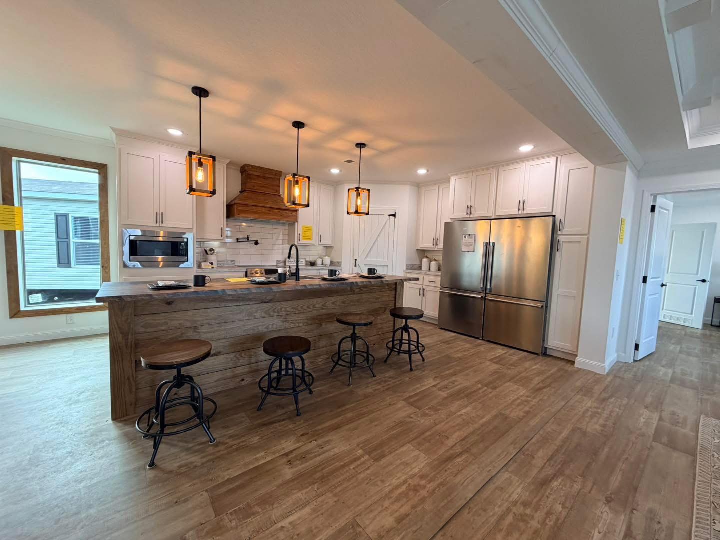 Modern kitchen with wooden floors, an island bar with four stools, pendant lights, and stainless steel appliances. Bright, inviting, and spacious.