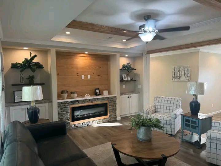 Modern living room with cozy decor. Features include a stone fireplace, wooden accents, plaid armchairs, a ceiling fan, and soft lighting.