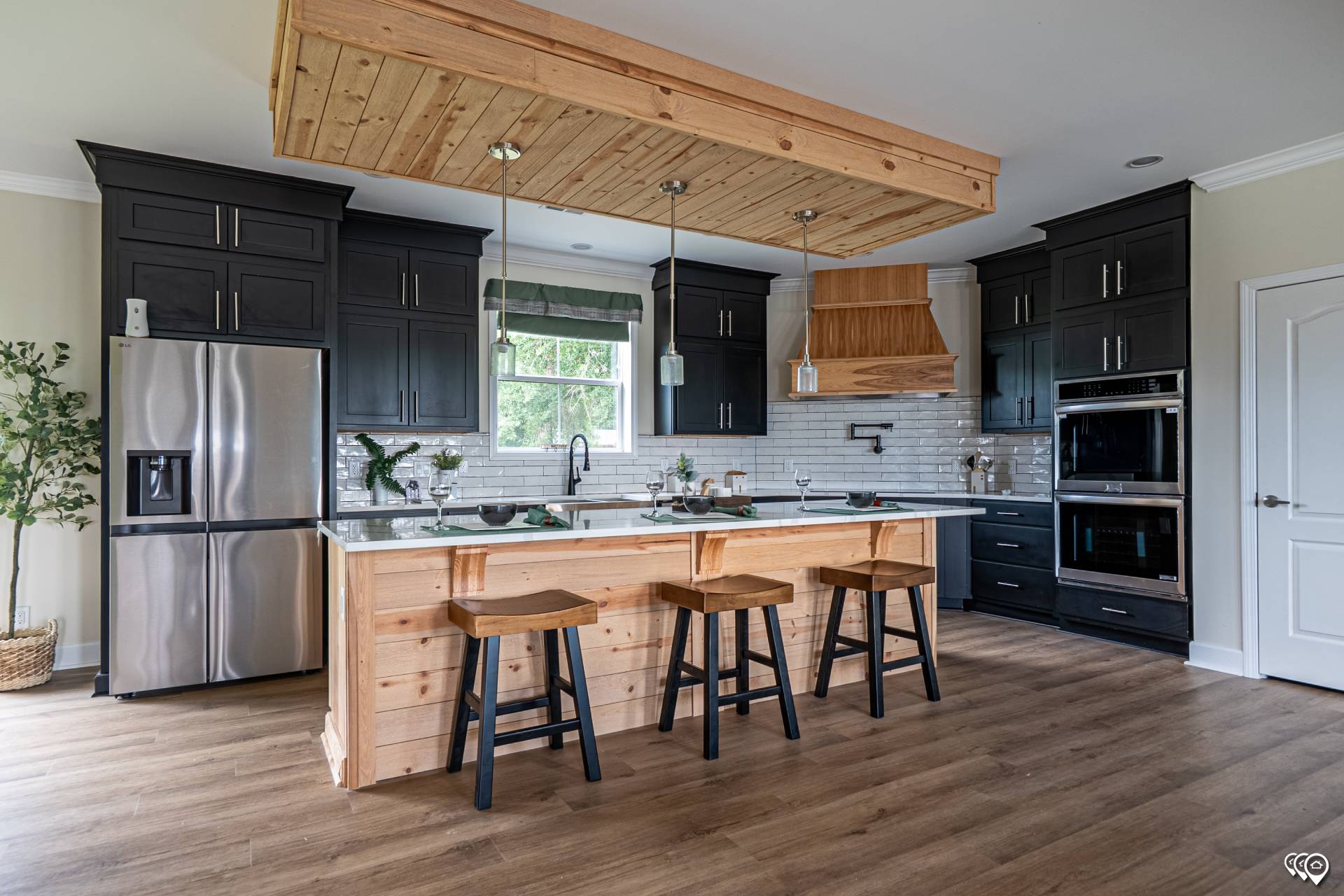 Spacious modern kitchen with black cabinets, stainless steel appliances, and wooden accents. Island with stools under pendant lights exudes warmth.