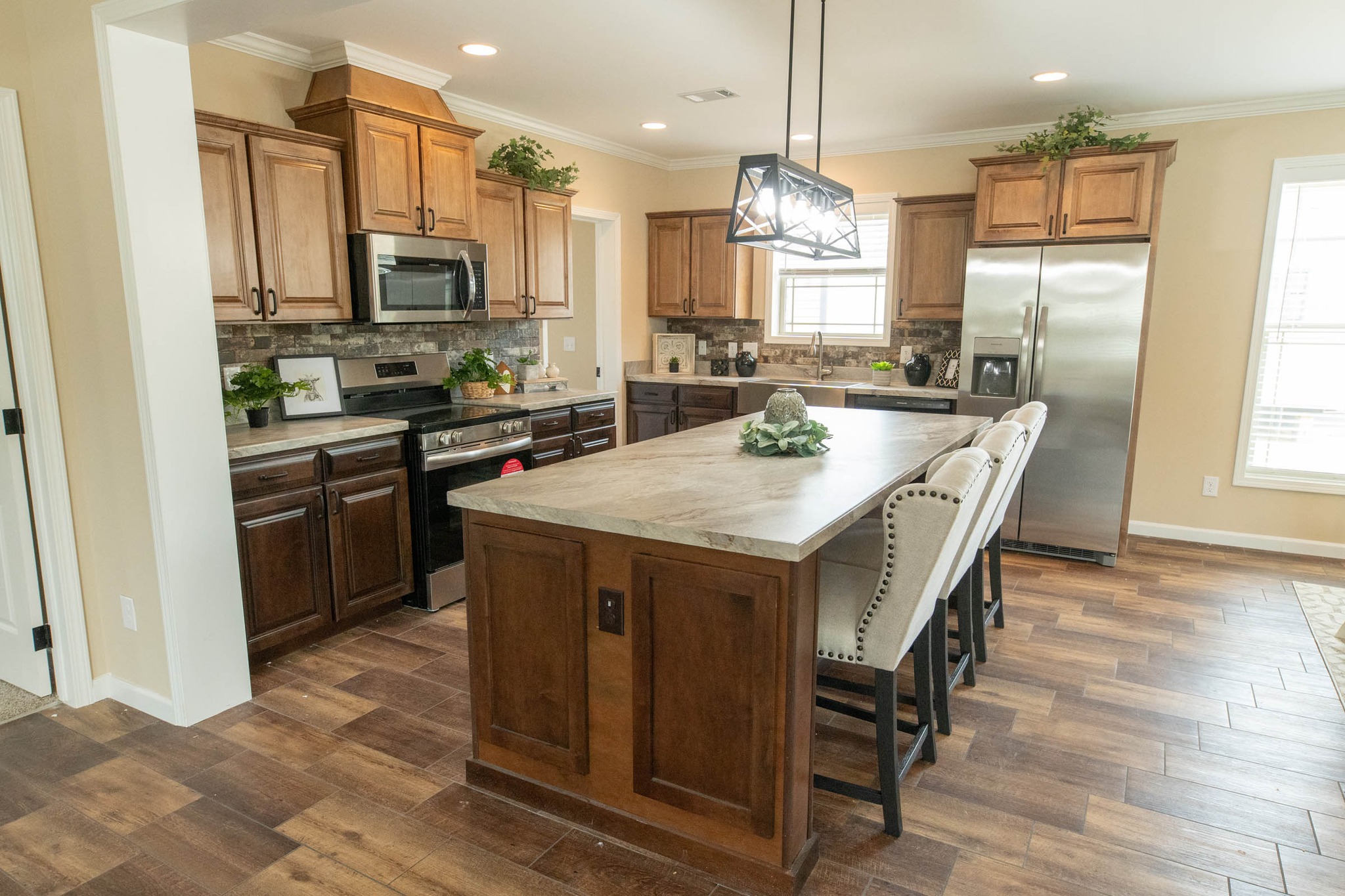 Spacious kitchen with wooden cabinets, a large island with beige countertops, cushioned chairs, stainless steel appliances, and warm lighting. Cozy, modern feel.