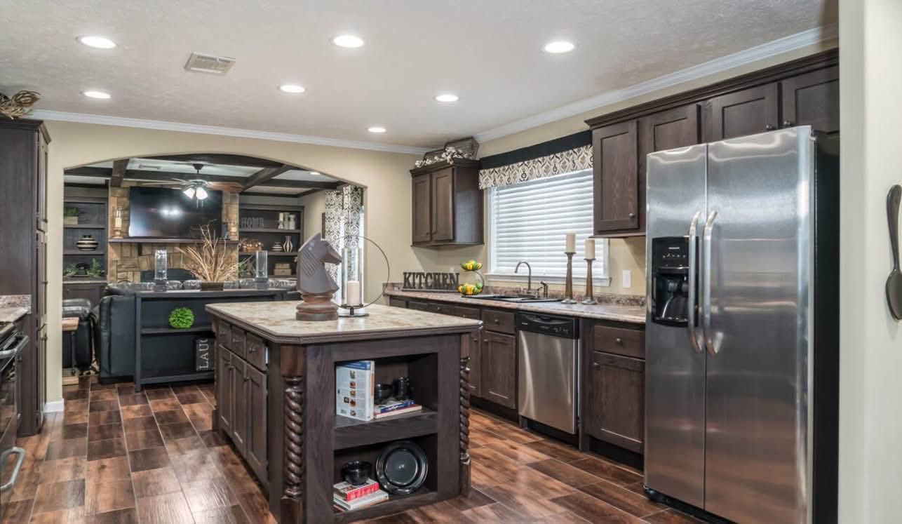 Spacious kitchen with dark wood cabinets, stainless steel appliances, and a central island. Warm lighting, adjacent to a cozy living area.