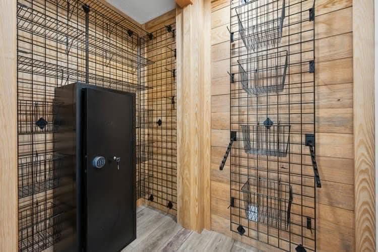 Wood-paneled room with black metal wire shelving and baskets. A black safe with a combination lock stands to the left. Tidy and secure ambiance.