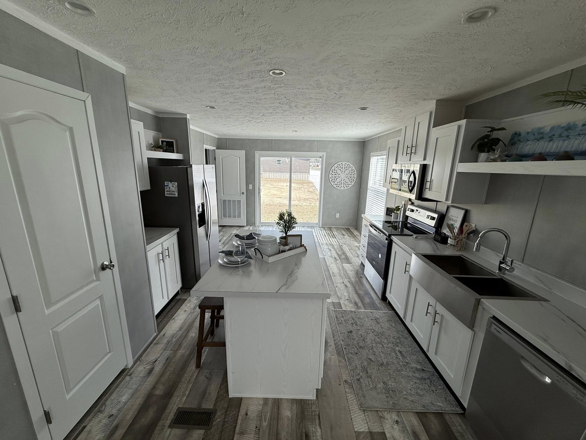 Modern kitchen with gray walls and wood flooring. Features a centered island with dishes, stainless steel appliances, and white cabinets conveying a clean, contemporary look.