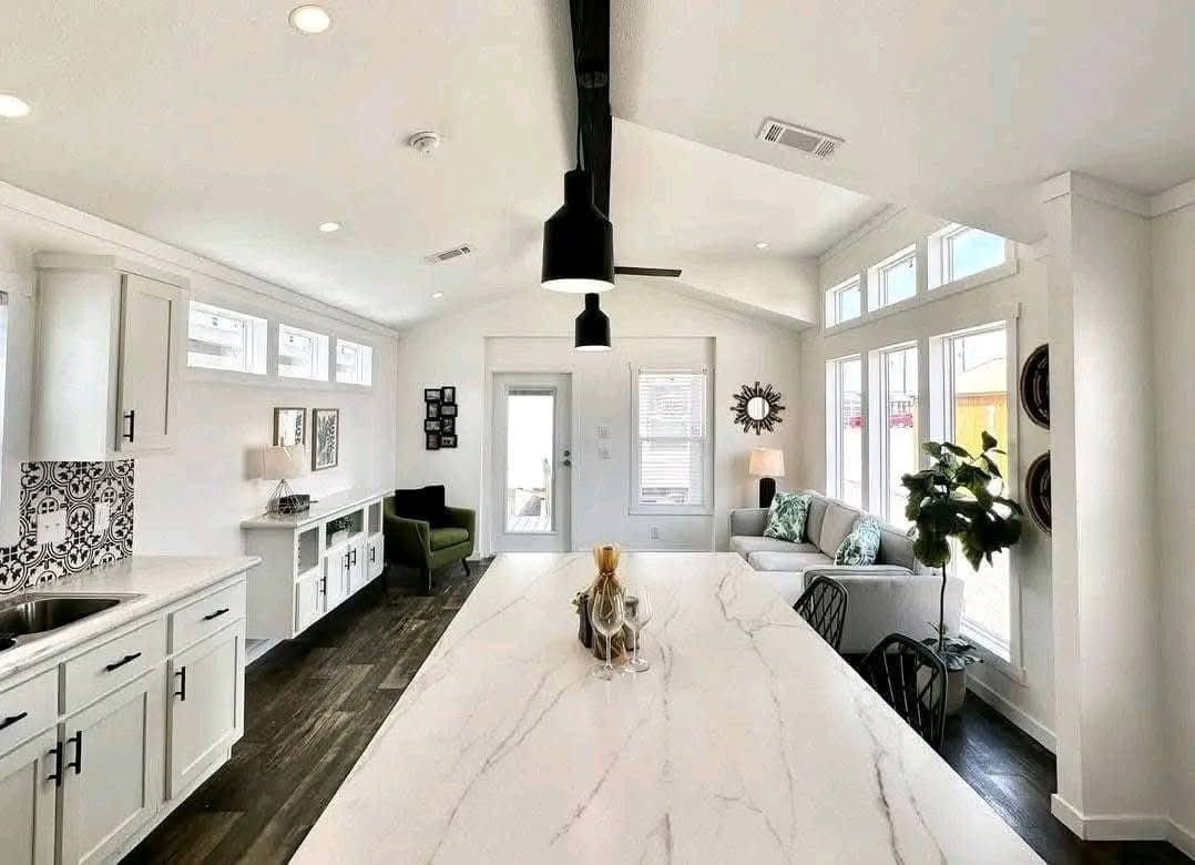 Modern open-concept kitchen and living area with white cabinetry, marble island, dark wood flooring, and large windows. Bright, cozy, and inviting.