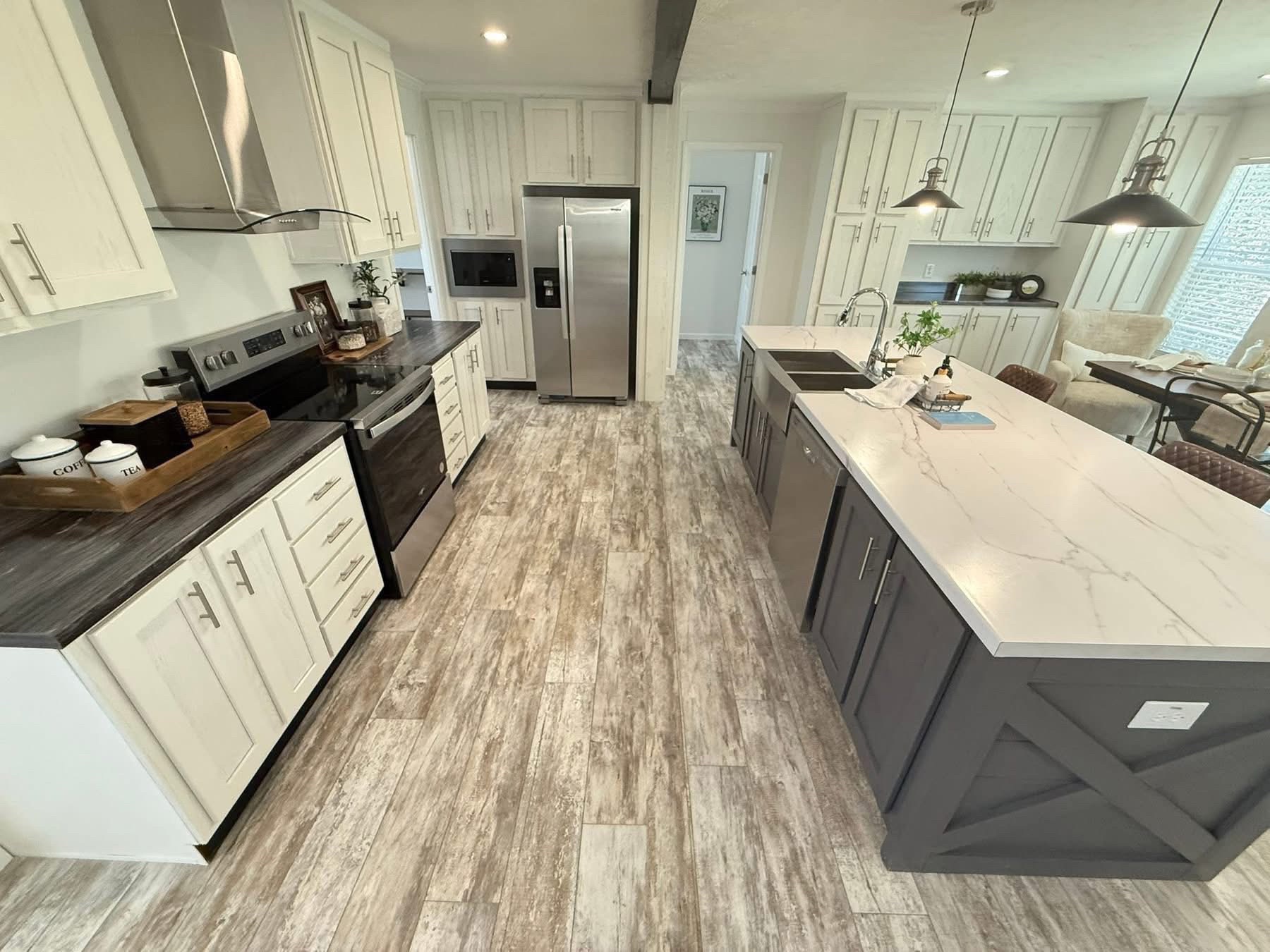 Spacious modern kitchen with wood and marble elements. Features large island, stainless steel appliances, and pendant lights, conveying elegance.