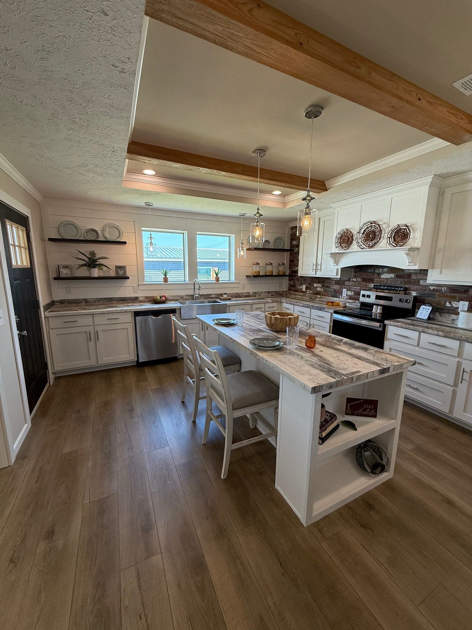 Modern kitchen with white cabinets, marble countertops, and a central island with bar stools. Warm lighting and wooden beams add a cozy feel.