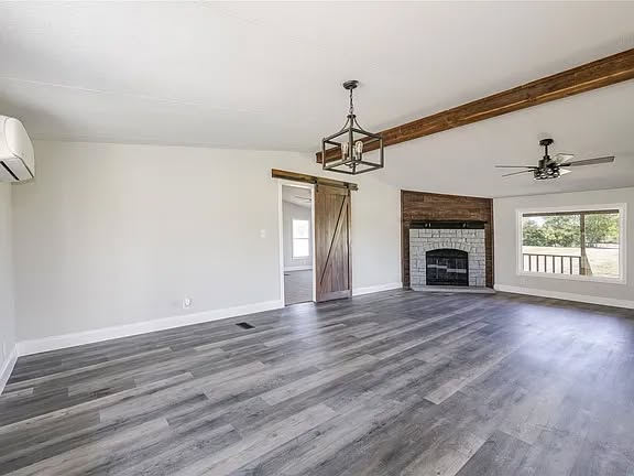 Spacious living room with light gray walls and wooden floors. Features a rustic sliding barn door, white brick fireplace, large window, and ceiling fan.