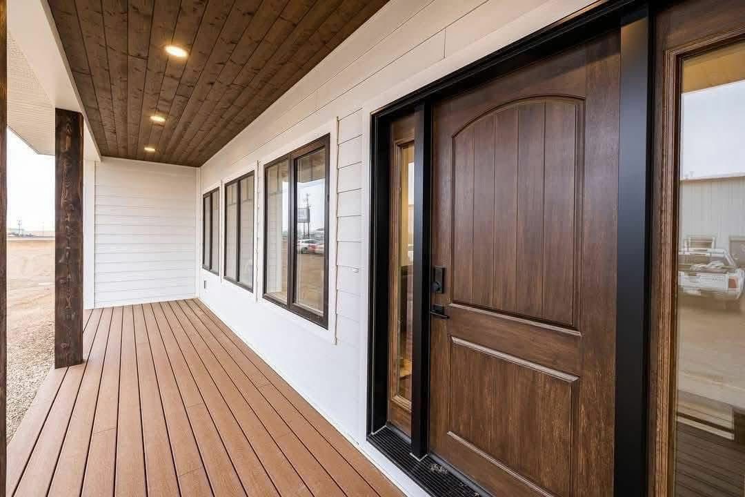 Modern porch view with a wooden floor and ceiling. Features a brown wooden door and several windows on a white wall, creating a warm, inviting atmosphere.