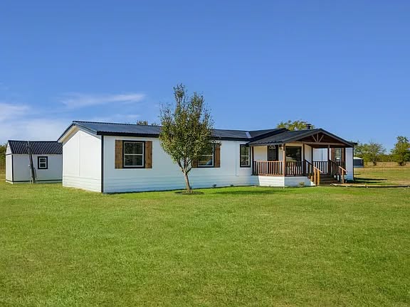 Single-story white house with a black roof and a small front porch, set in a vibrant green lawn under a clear blue sky, conveying a peaceful rural vibe.