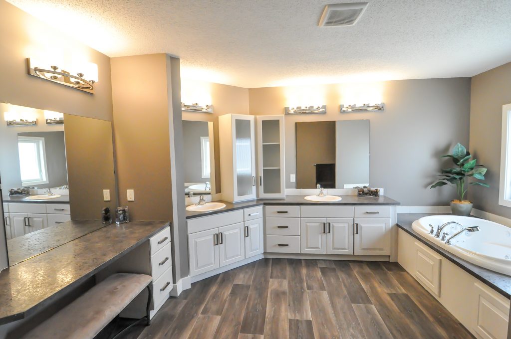 Modern bathroom interior with a neutral palette, featuring a corner vanity with dual sinks, large mirrors, a soaking tub, bright lighting, and wood floors.