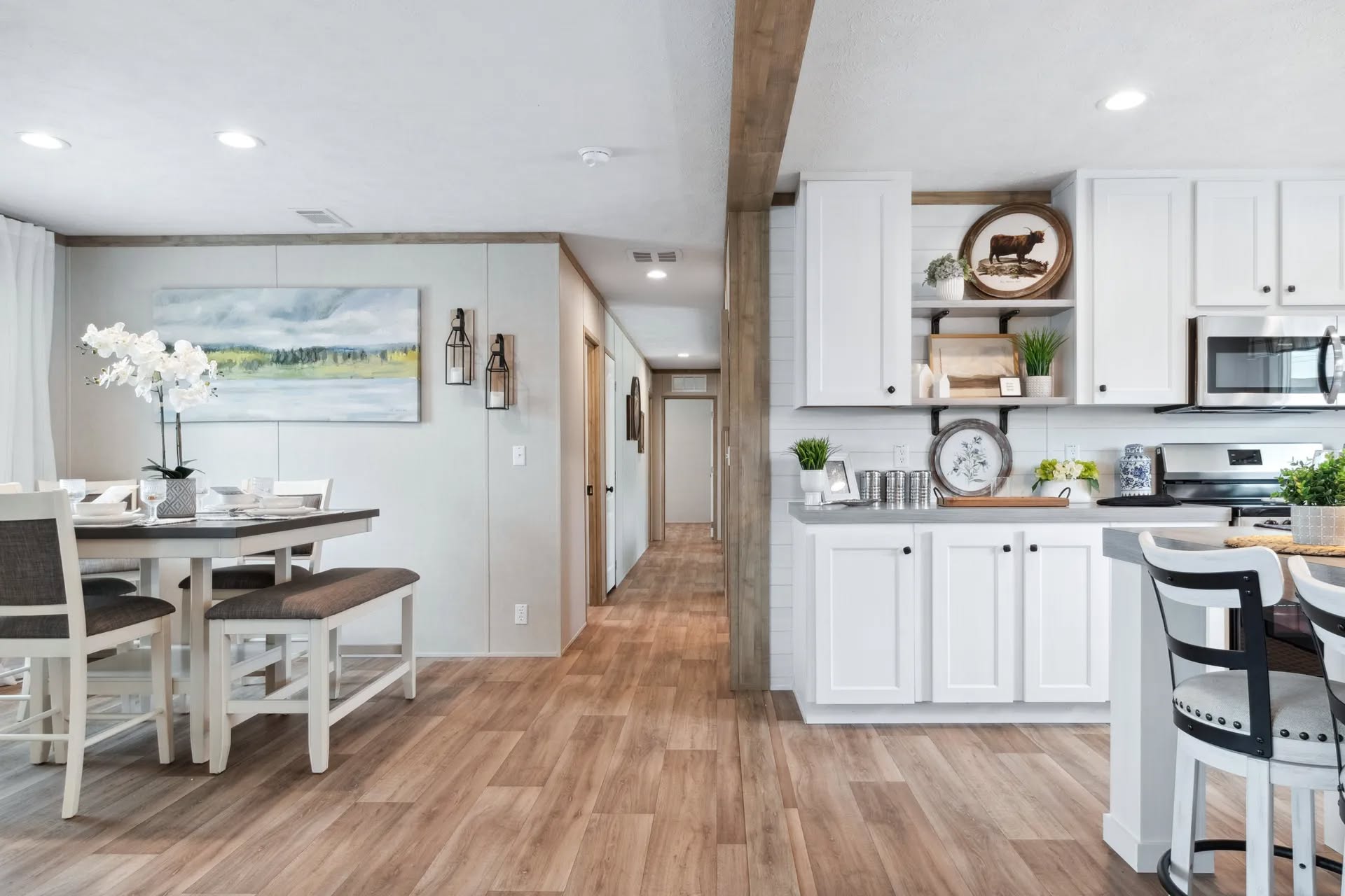 Bright open kitchen and dining area with white cabinets, wooden floors, and modern decor. A round dining table with chairs is on the left, under soft lighting, creating a cozy ambiance.