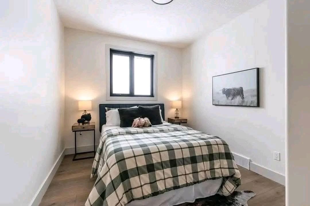 A cozy bedroom with a plaid-patterned bedspread, two bedside tables with lamps, and a black and white cow art piece on the wall, creating a warm, rustic feel.