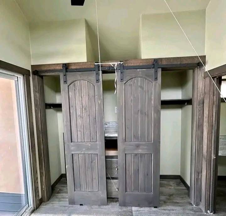 Gray wooden sliding closet doors on black metal tracks reveal an unfinished interior and a piece of furniture. The room has a modern, minimalist design.