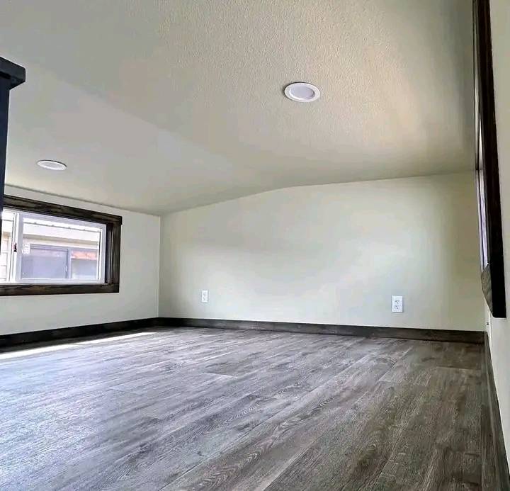 Small, minimalist attic room with light wood flooring and beige walls. A large window on the left lets in natural light, creating a cozy, airy feel.