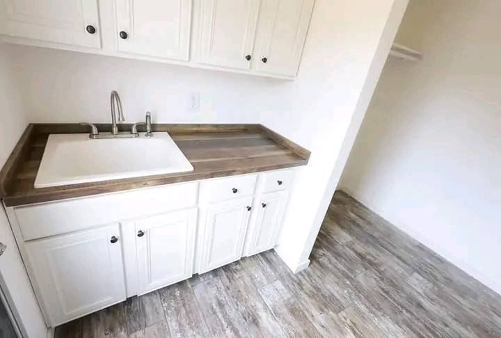 Laundry room with white cabinets and a wooden countertop. A large sink is set in the counter. Light wood flooring creates a clean, minimalist look.