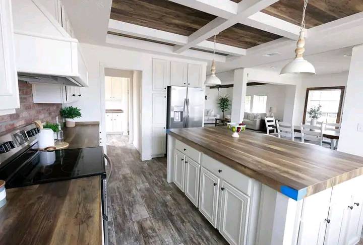 Spacious modern kitchen with a large wooden island, white cabinets, and stainless steel appliances. Pendant lights hang above, creating a cozy vibe.