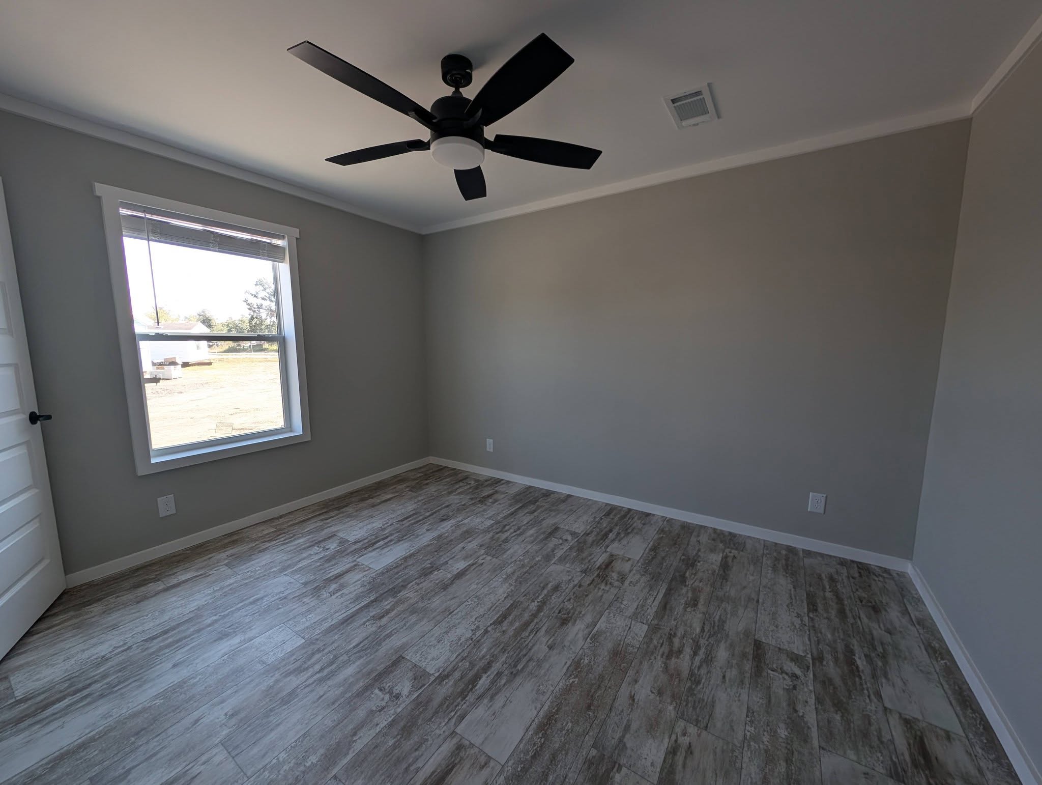 Empty room with light gray walls, a large window, and wood-look tile flooring. A black ceiling fan is centered on the white ceiling, creating a modern feel.