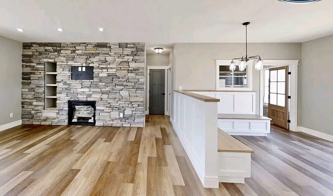 Modern living room with stone accent wall, built-in shelves, and a fireplace. Light wood flooring and a white partition beneath elegant pendant lights.
