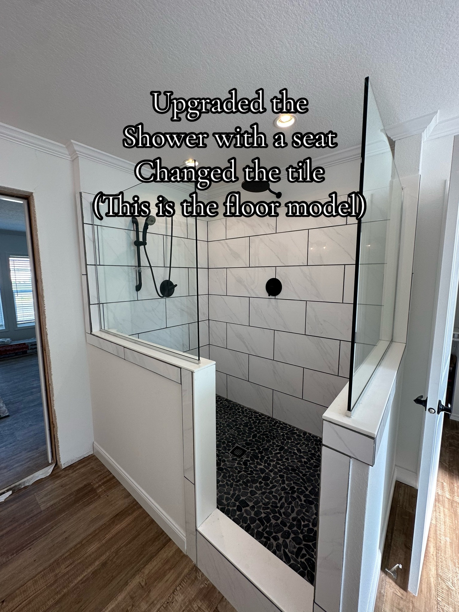 Modern shower upgrade with a seat and new tile. Features white walls, black fixtures, and pebble flooring. Text overlay describes changes.