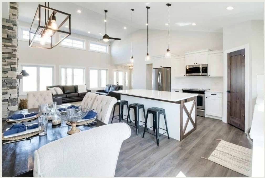 Modern open-concept kitchen and living room with high ceilings, pendant lights, a large island with stools, and a cozy dining area with elegant settings.