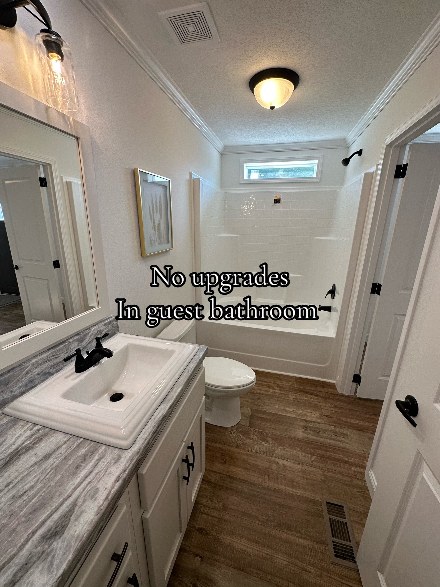 Modern guest bathroom featuring white fixtures, a marble countertop, wood-style flooring, and minimal decor; a text overlay reads "No upgrades in guest bathroom."