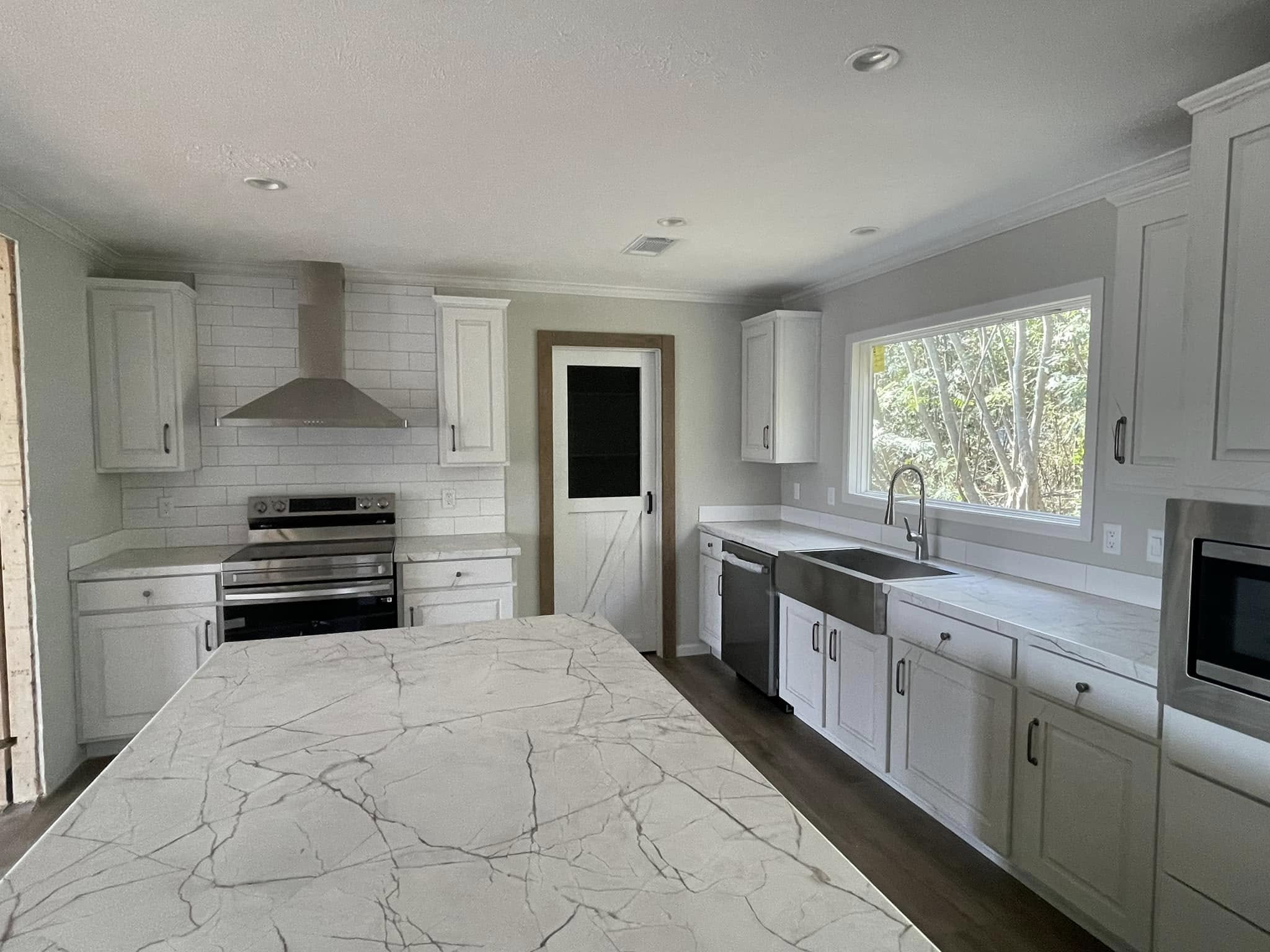 Modern kitchen with white cabinets, marble island countertop, stainless steel appliances, and large window. Bright, clean, and spacious atmosphere.