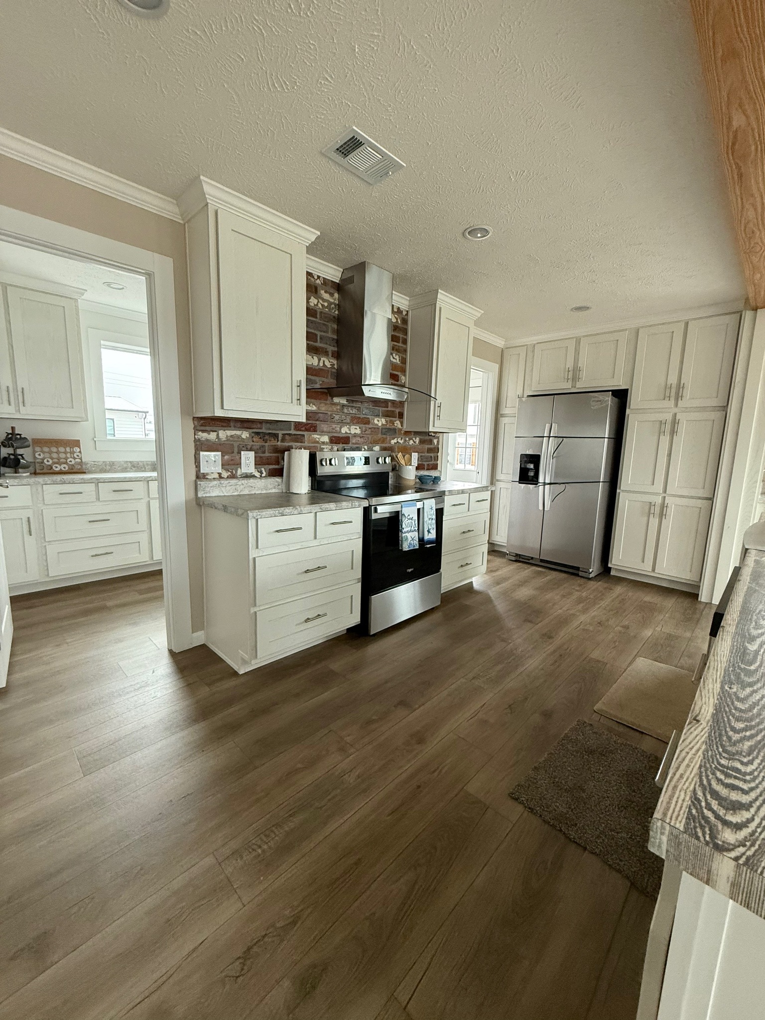 Modern kitchen with white cabinets, stainless steel appliances, and a brick backsplash. Light wood flooring and neutral tones create a cozy feel.