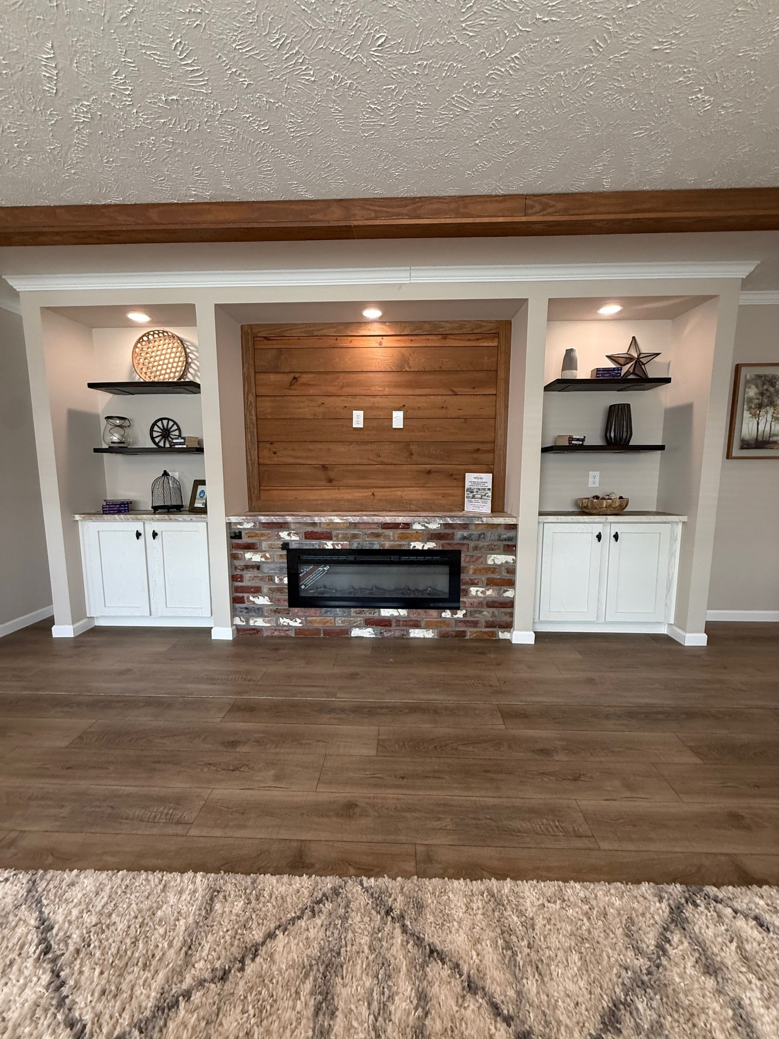 A cozy living room features a rustic wood and brick fireplace set between two white shelves with decorative items. Warm lighting and a plush carpet create an inviting ambiance.