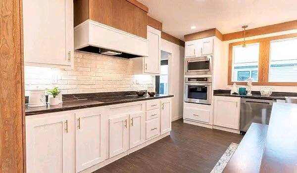 Bright, modern kitchen with white cabinets, dark countertops, and wood accents. Stainless steel appliances, large windows, and a warm, inviting feel.