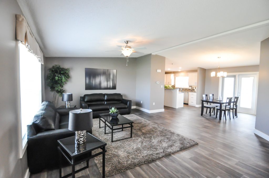 Modern living and dining area with sleek black leather sofas and abstract art on gray walls. A plush rug, dining set, and open kitchen evoke a cozy, contemporary feel.