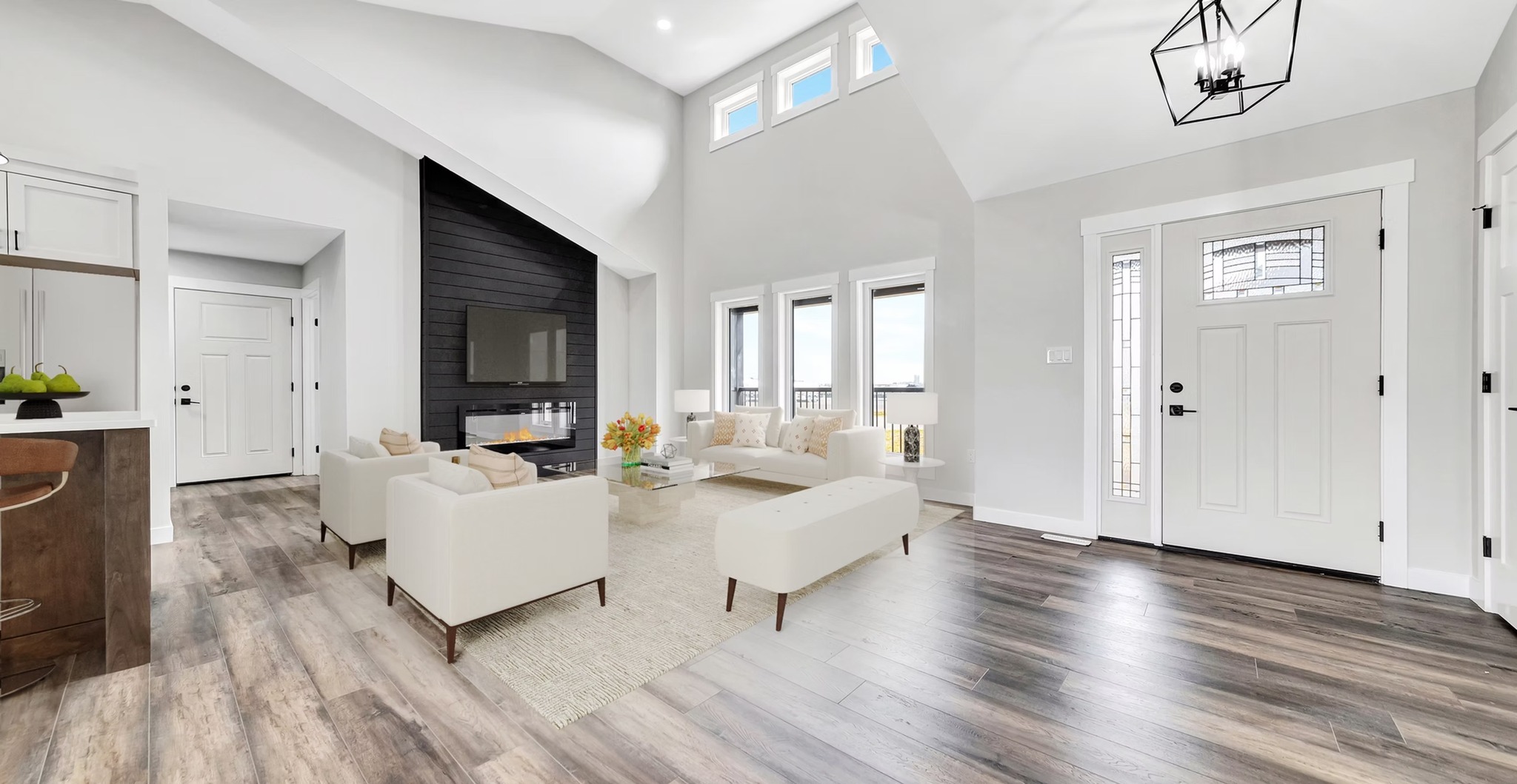 Bright contemporary living room with high ceiling, white walls, and wood floors. Features beige sofas, a fireplace, and large windows with a view.