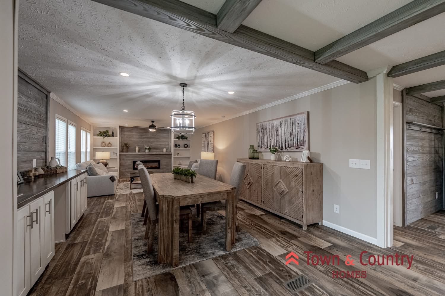 Spacious open-plan dining and living area with rustic wood accents, cozy fireplace, natural light through windows, and elegant decor creating a warm ambiance.
