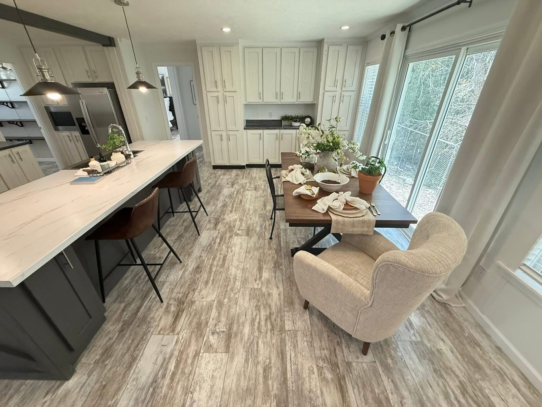 Spacious kitchen with white cabinets, rustic wood flooring, and a marble island. Dining area features a table set for guests. Bright and welcoming.